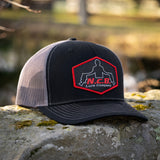 A black/charcoal NCB patch style snapback hat positioned on a rock